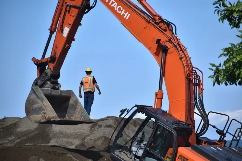 Construction worker with an excavator on a dirt mound, clear blue sky.