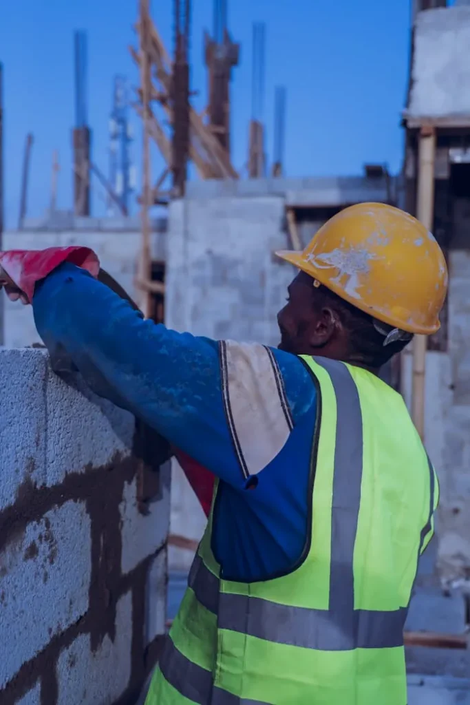 Construction worker in safety gear building a concrete wall at an outdoor site.